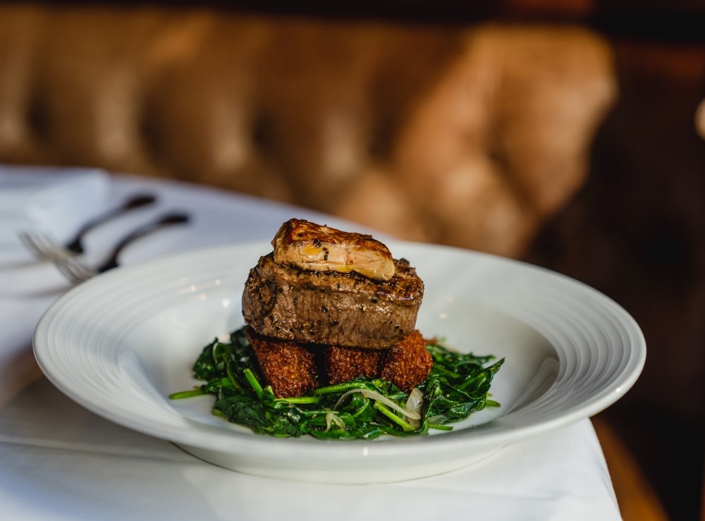 Chef prepared meal with meat on a bed of greens on white plate on white tablecloth