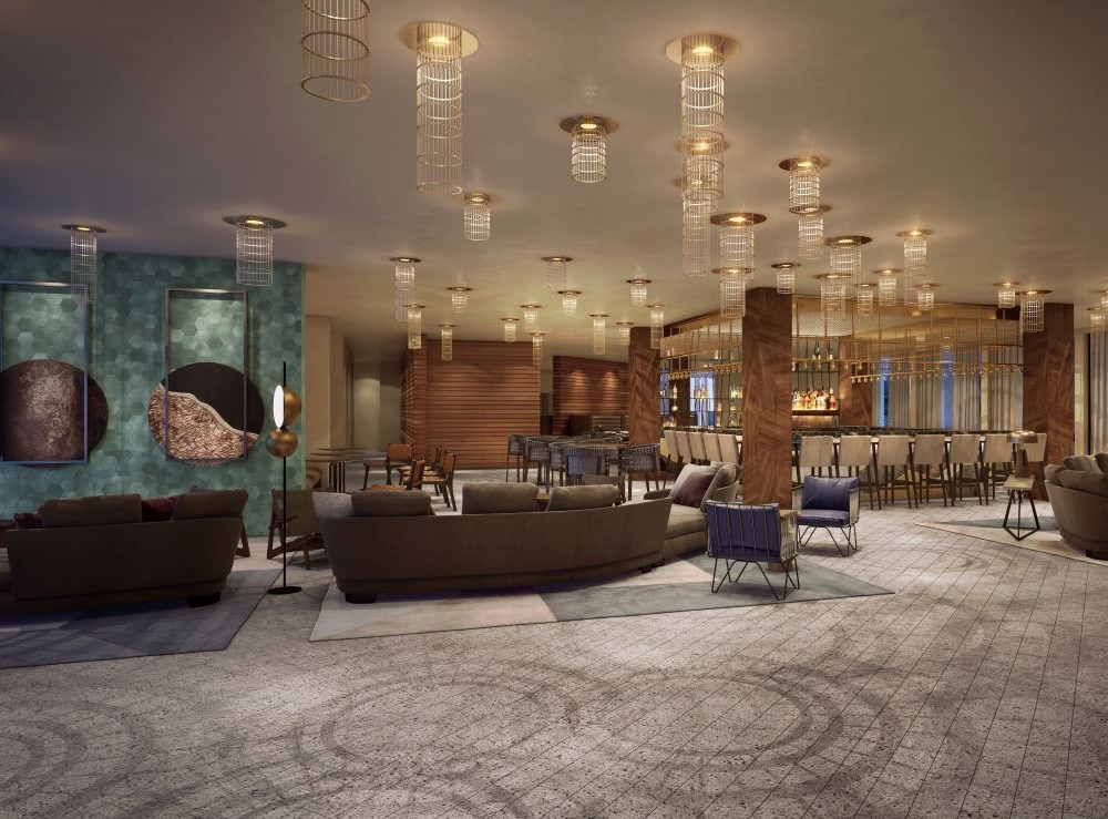 A hotel lobby with contemporary brown, tan, and blue furnishings with a square bar in the far corner and spiral lights hanging from the ceiling.