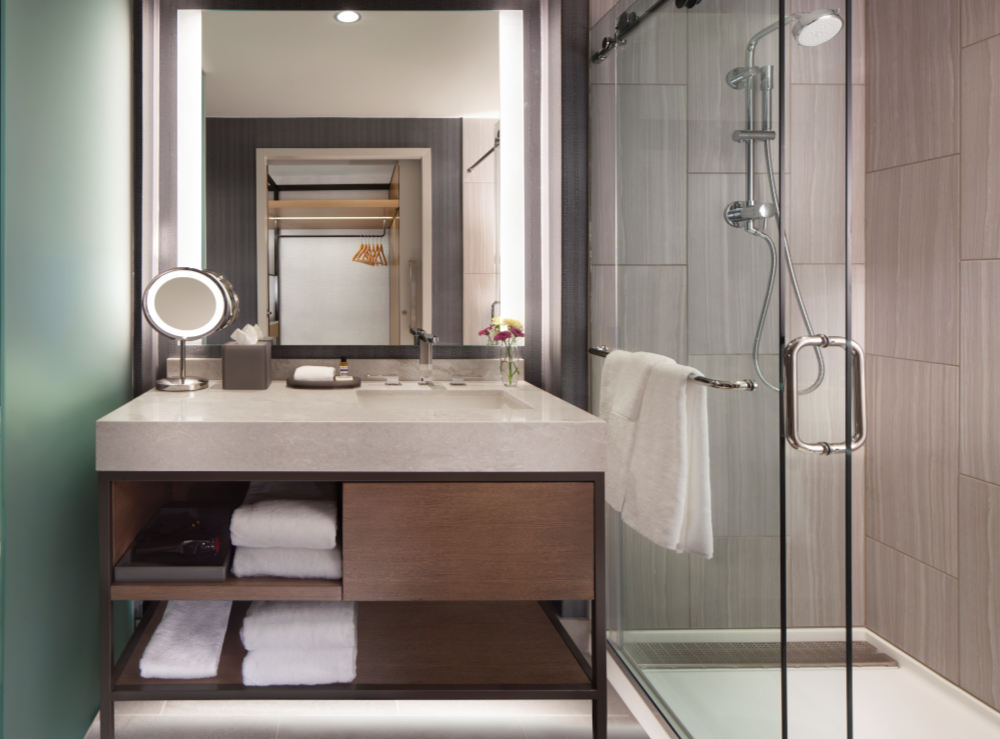 A hotel guestroom contemporary bathroom with sink, lighted mirror, and shower
