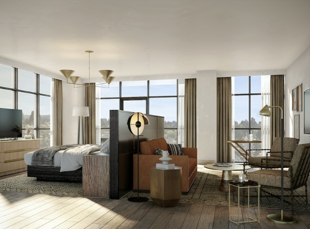 A hotel suite in a studio setting with large windows is decorated with modern earth toned decor.