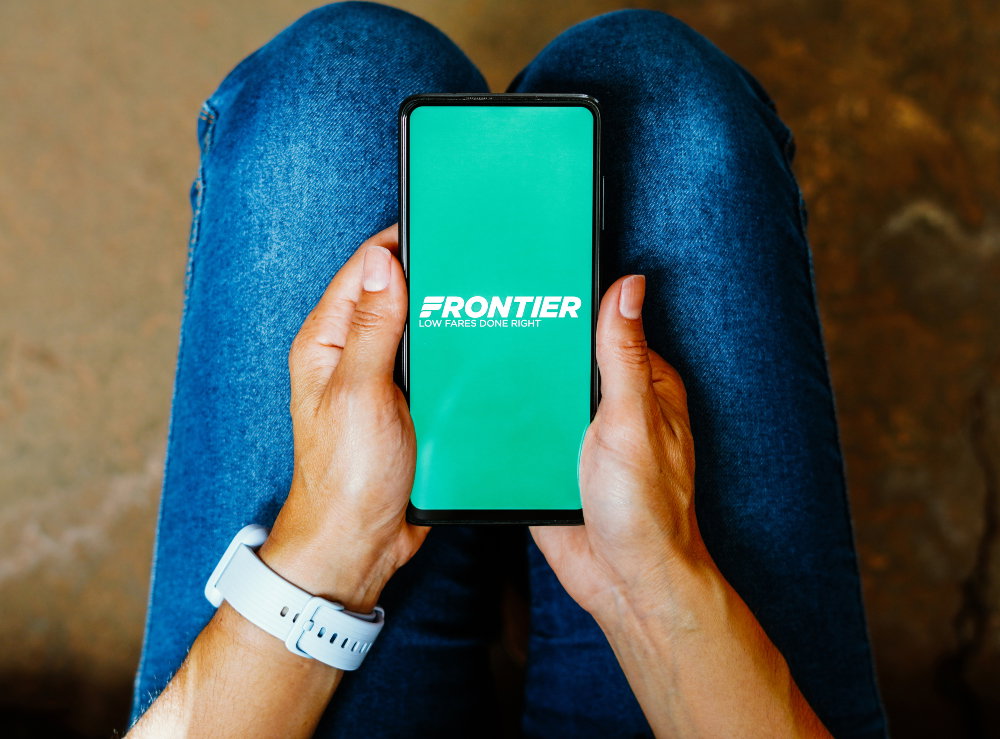 A person holds a mobile phone displaying Frontier Airlines' logo
